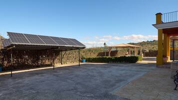 A covered outdoor area with solar panels, a concrete patio, and a building with a yellow facade.