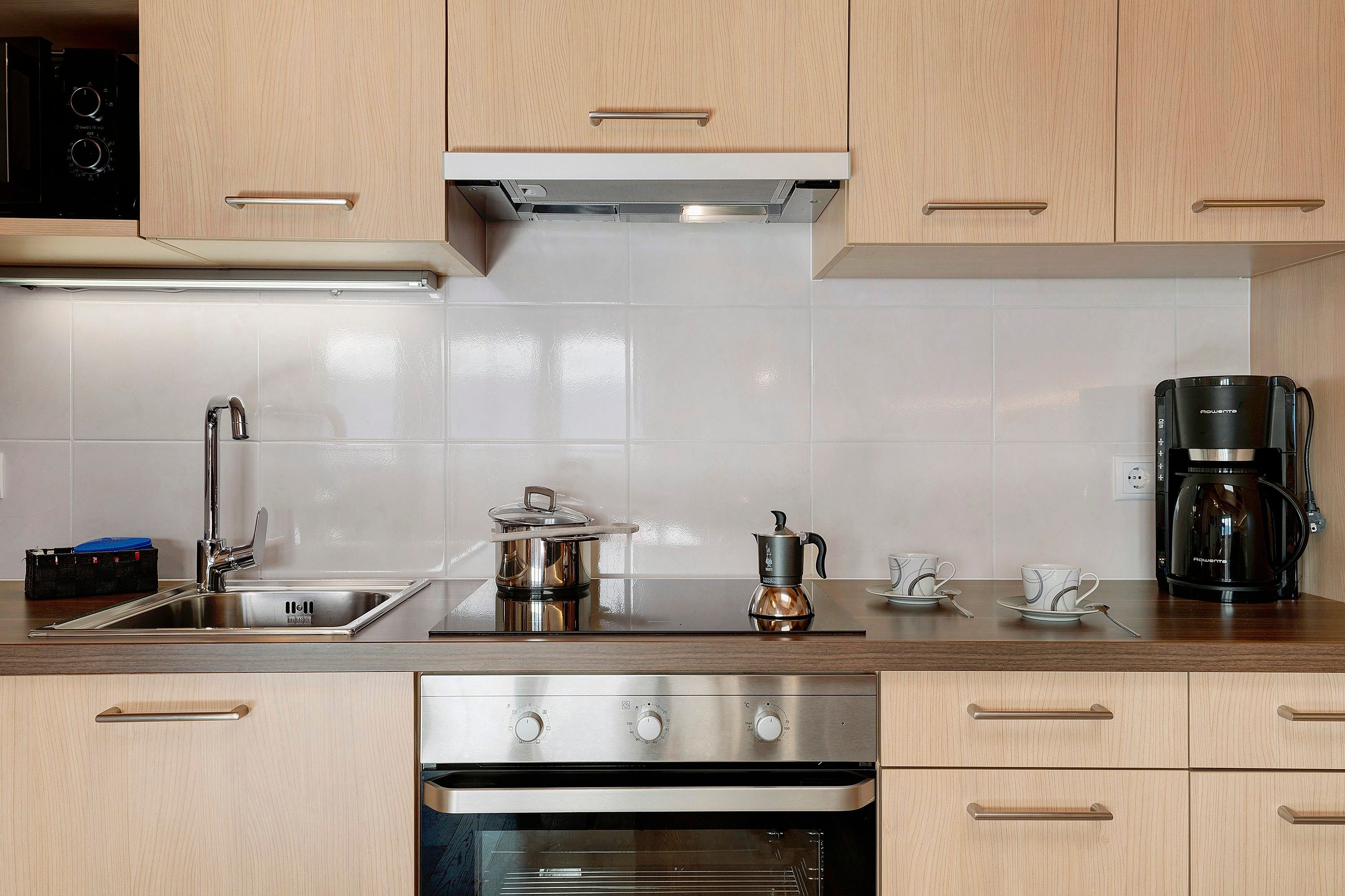 Una cocina moderna con electrodomésticos de acero inoxidable, una cafetera y un hervidor sobre la encimera.