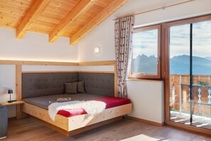 A bedroom with a wooden ceiling, a sofa bed, a window with curtains, and a view of mountains.