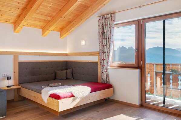 Un dormitorio con techo de madera, sofá cama, ventana con cortinas y vistas a montañas.