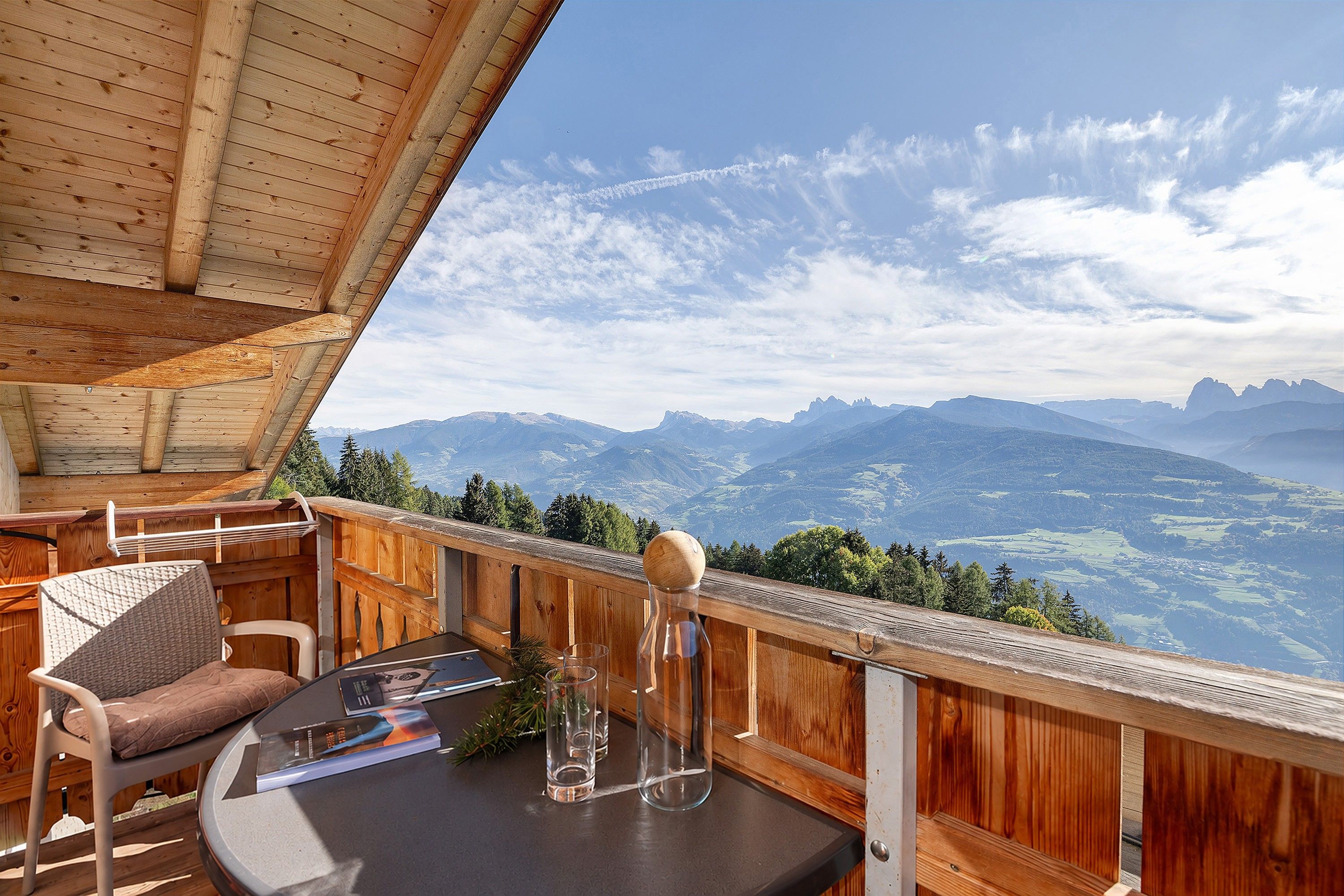 Una terraza de madera con vista a montañas, una mesa con un vaso y una silla.