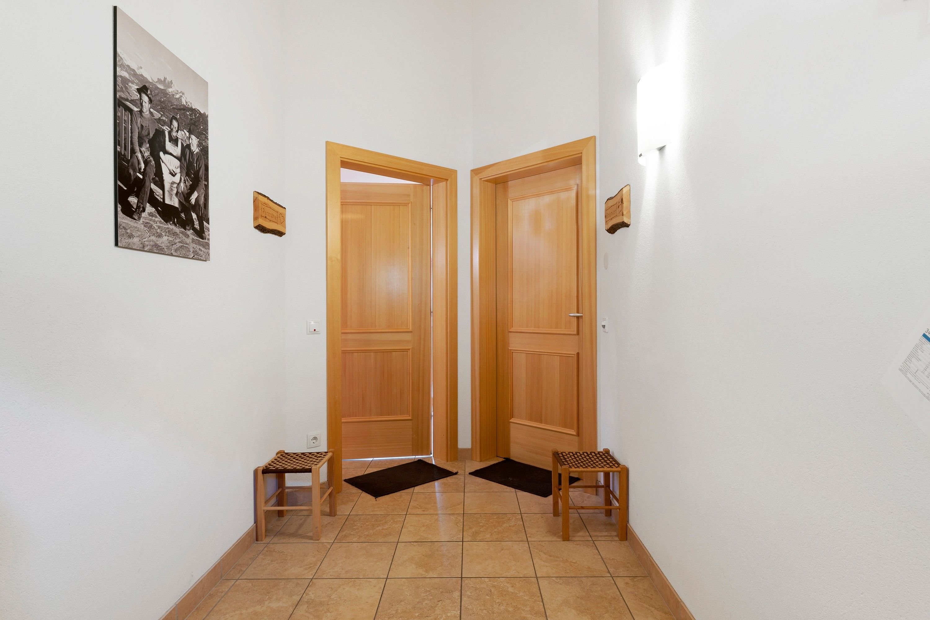 Un pasillo con dos puertas de madera, una fotografía blanco y negro en la pared y dos taburetes de madera.