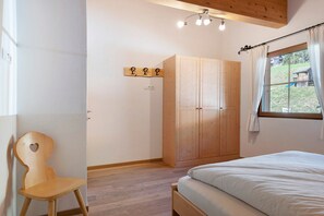 A bedroom with a wooden bed, a wooden wardrobe, a wooden chair, and a window with a view of the outdoors.