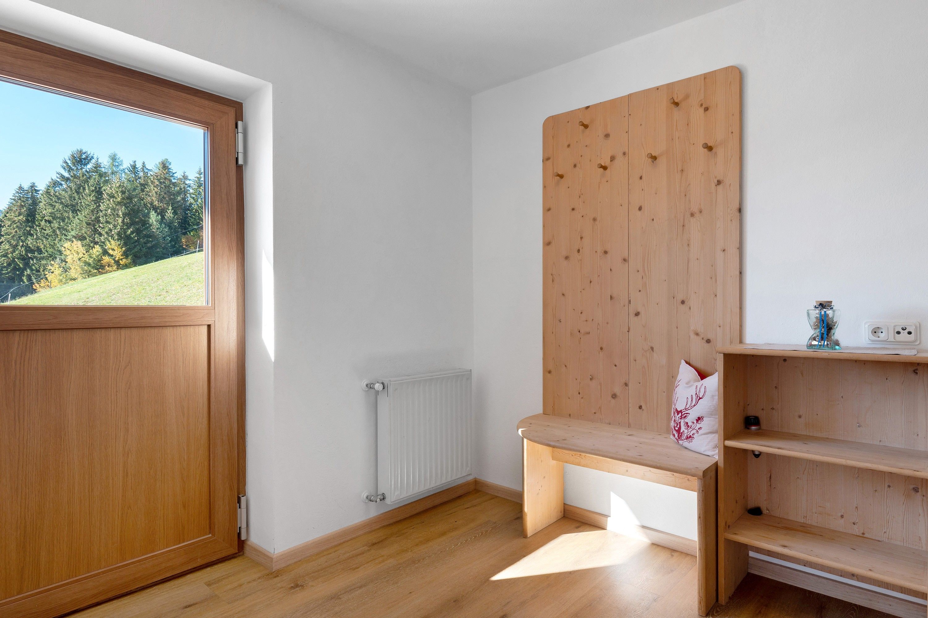A room with a wooden door, a radiator, a bench, and a shelf with a decorative pillow.