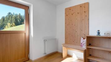 A room with a wooden door, a radiator, a bench, and a shelf with a decorative pillow.