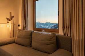 Ein gemütliches Zimmer mit einer Couch, einem Fenster mit Vorhängen, einem Heizkörper und einem Holzbalken mit Seil.
