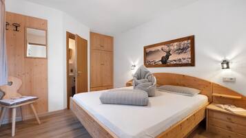 A bedroom with a wooden bed, a chair, a bedside table, a nightstand, and a wall-mounted picture.
