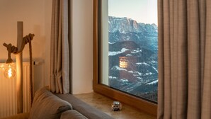 Une pièce dotée d’une grande fenêtre, d’un plancher en bois, d’un canapé, d’une lampe et offrant une vue sur des montagnes enneigées.