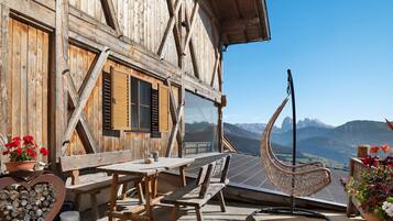 Un chalet de madera con comedor, un leñedo con forma de corazón y vistas a la montaña.