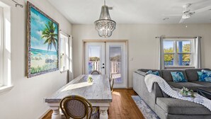 A dining area with a wooden table and chairs, a chandelier, and a painting of a beach scene. - Relaxing Beach Escape w/ Private Decks Walk2Beach (Galveston)