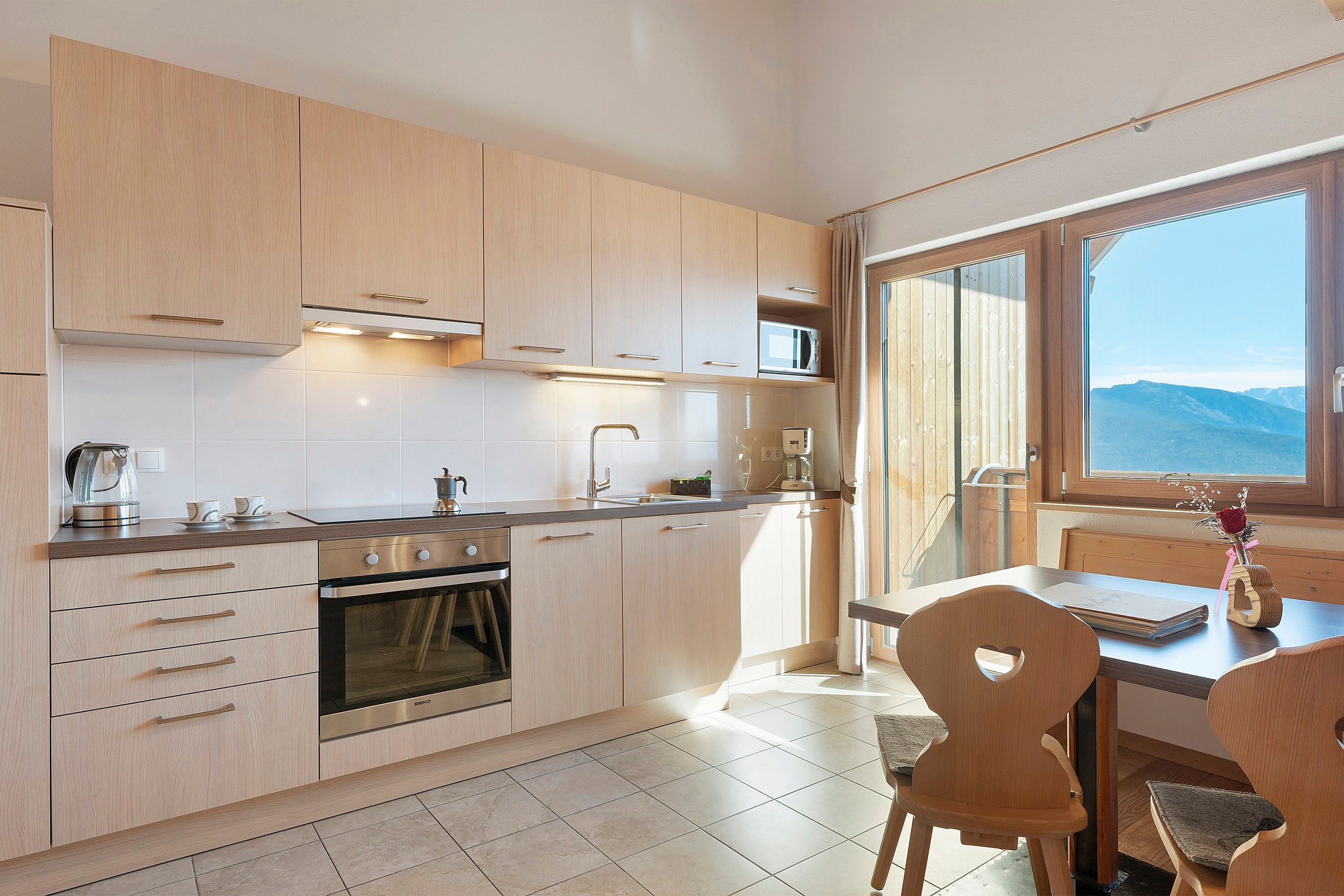 A modern kitchen with wooden cabinets, a built-in oven, and a dining area with a view of the mountains.