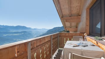 A balcony with a wooden railing, a table with a white tablecloth, and a view of mountains.