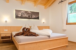 Un lit en bois avec des oreillers, une table de chevet, un tableau accroché au mur et une fenêtre avec des rideaux.