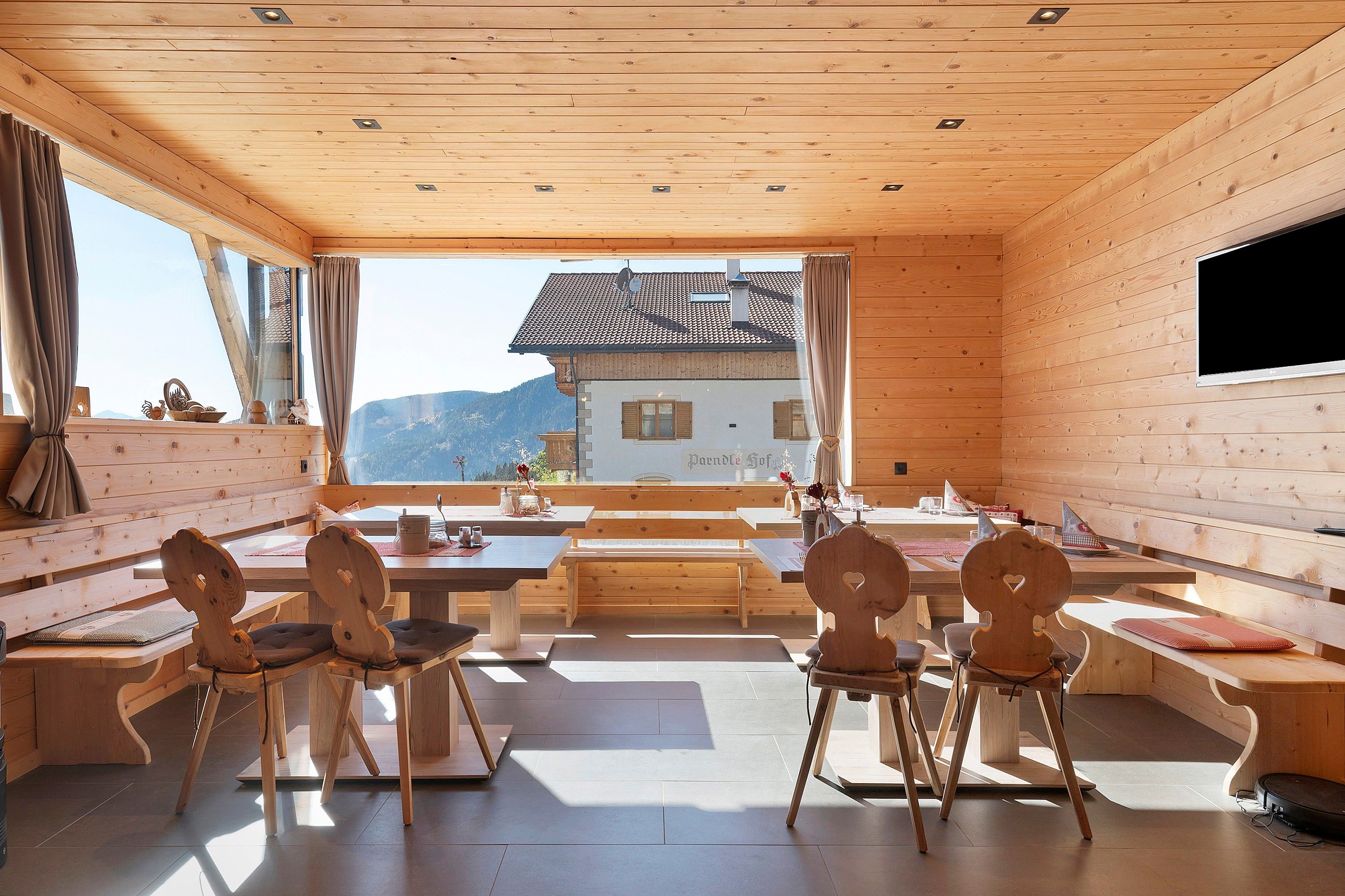 Interior de madera con comedor, bancos y vistas a la montaña.