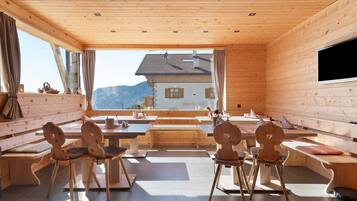 A wooden interior with a dining area, benches, and a view of a mountain.
