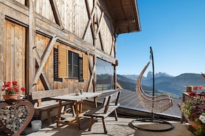 A wooden chalet with a dining area, a heart-shaped woodpile, and a view of mountains.