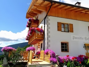 A traditional wooden building with a balcony adorned with flowers, a clear sky, and a mountain in the background.