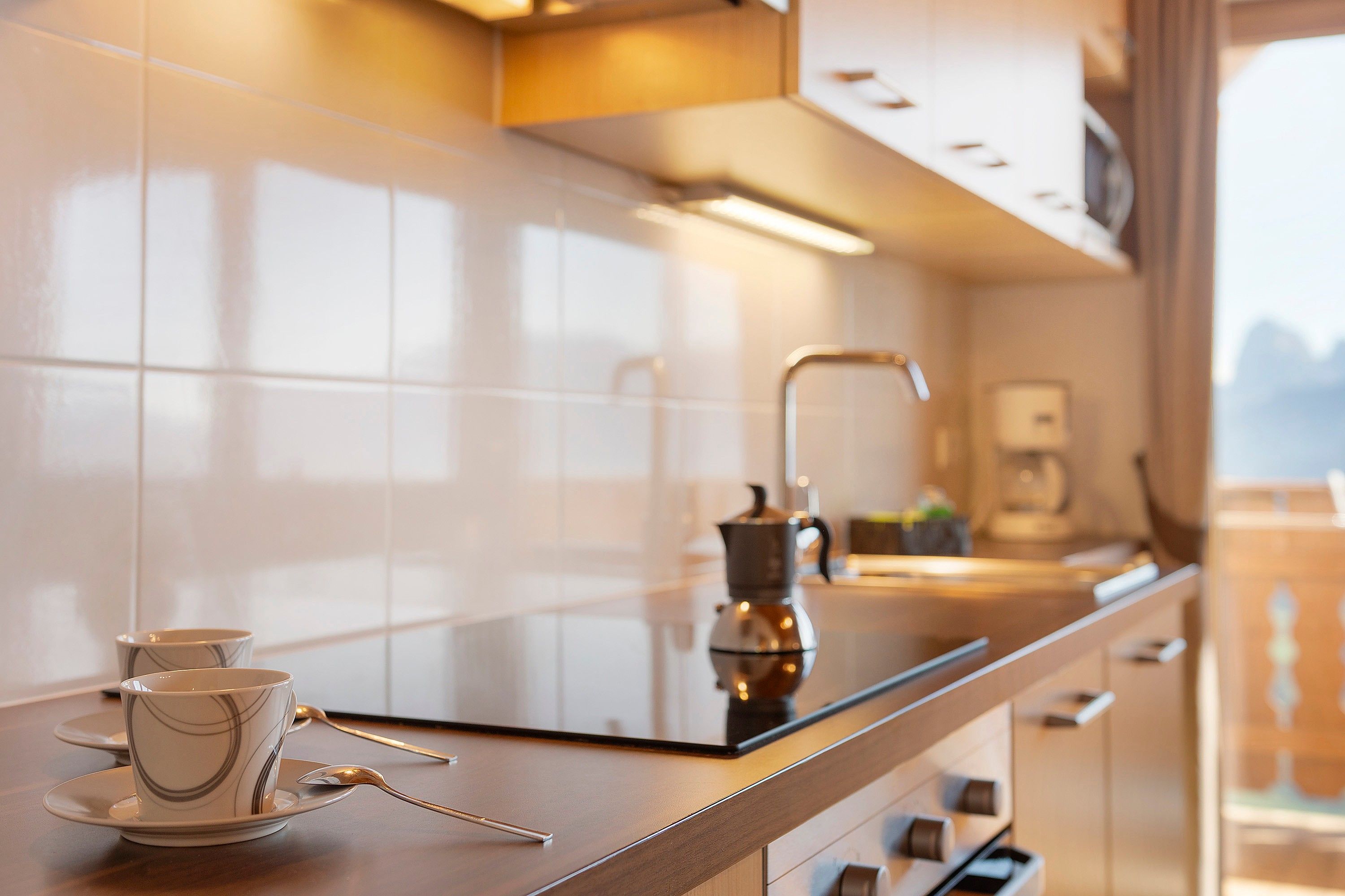 Una cocina moderna con encimera de vidrio, cafetera y vistas a las montañas.