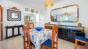 Un coin repas avec une table dressée pour quatre personnes, des chaises, un buffet orné de panneaux décoratifs, un grand miroir et un luminaire suspendu.
