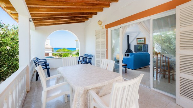 Un espace extérieur abrité, aménagé pour les repas, avec une table et des chaises, une vue sur la mer et un canapé bleu en arrière-plan.