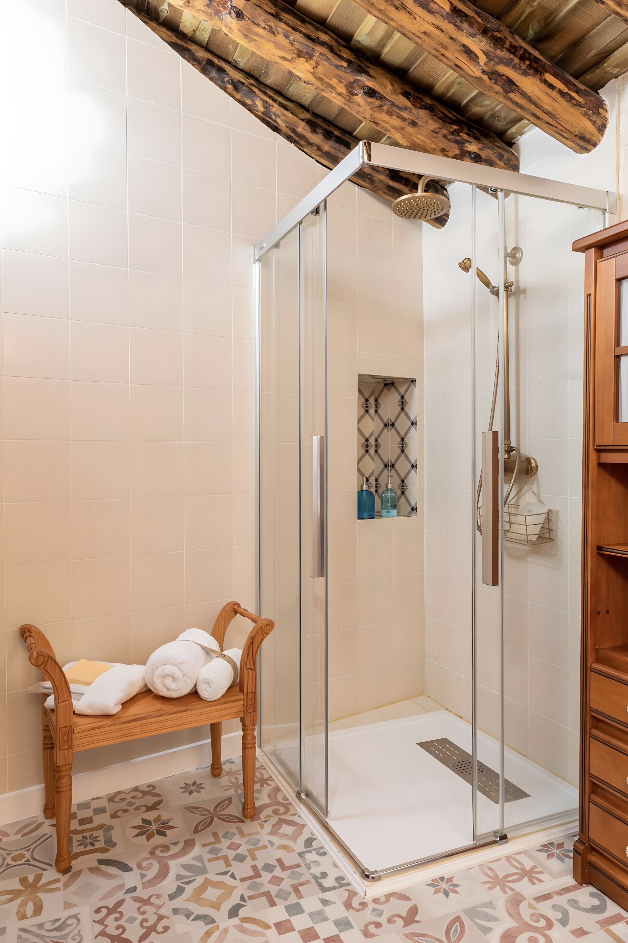 A shower area with a glass door, a bench with towels, and a patterned floor.