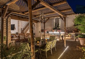 Un patio al aire libre con una pérgola de madera, una mesa con sillas y un muro de piedra.