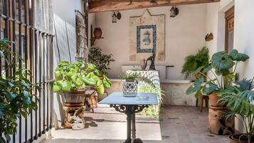 Un patio con mesa, sillas, plantas en macetas, una pérgola y suelo de baldosas.