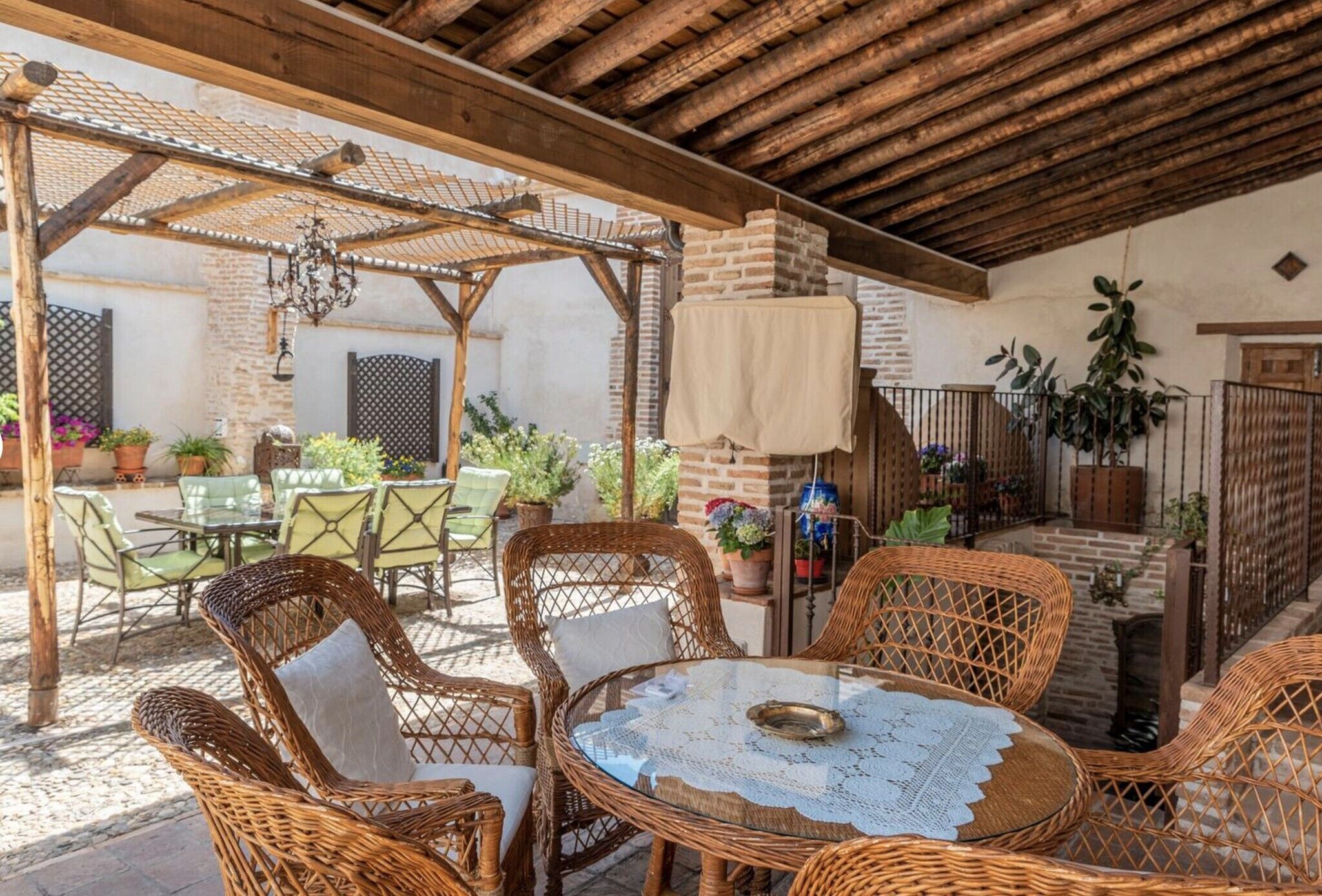 An outdoor patio with wicker furniture, a brick fireplace, and potted plants.