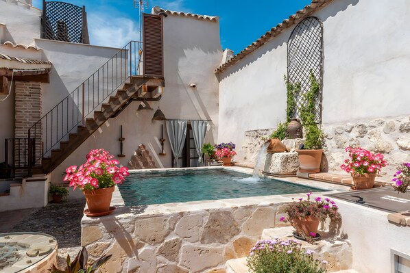 Une cour avec une piscine, des murs en pierre, un escalier et des plantes en pot.