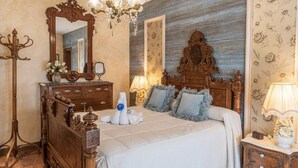 Une chambre à coucher avec un grand lit à baldaquin décoré, un lustre, un miroir et un papier peint à motifs floraux.