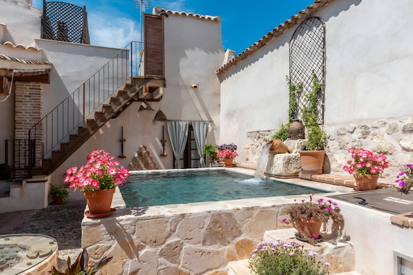 Une cour avec une piscine, des murs en pierre, un escalier et des plantes en pot.