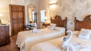 A hotel room with two beds, a wooden wardrobe, a mirror, and a floral wallpaper.