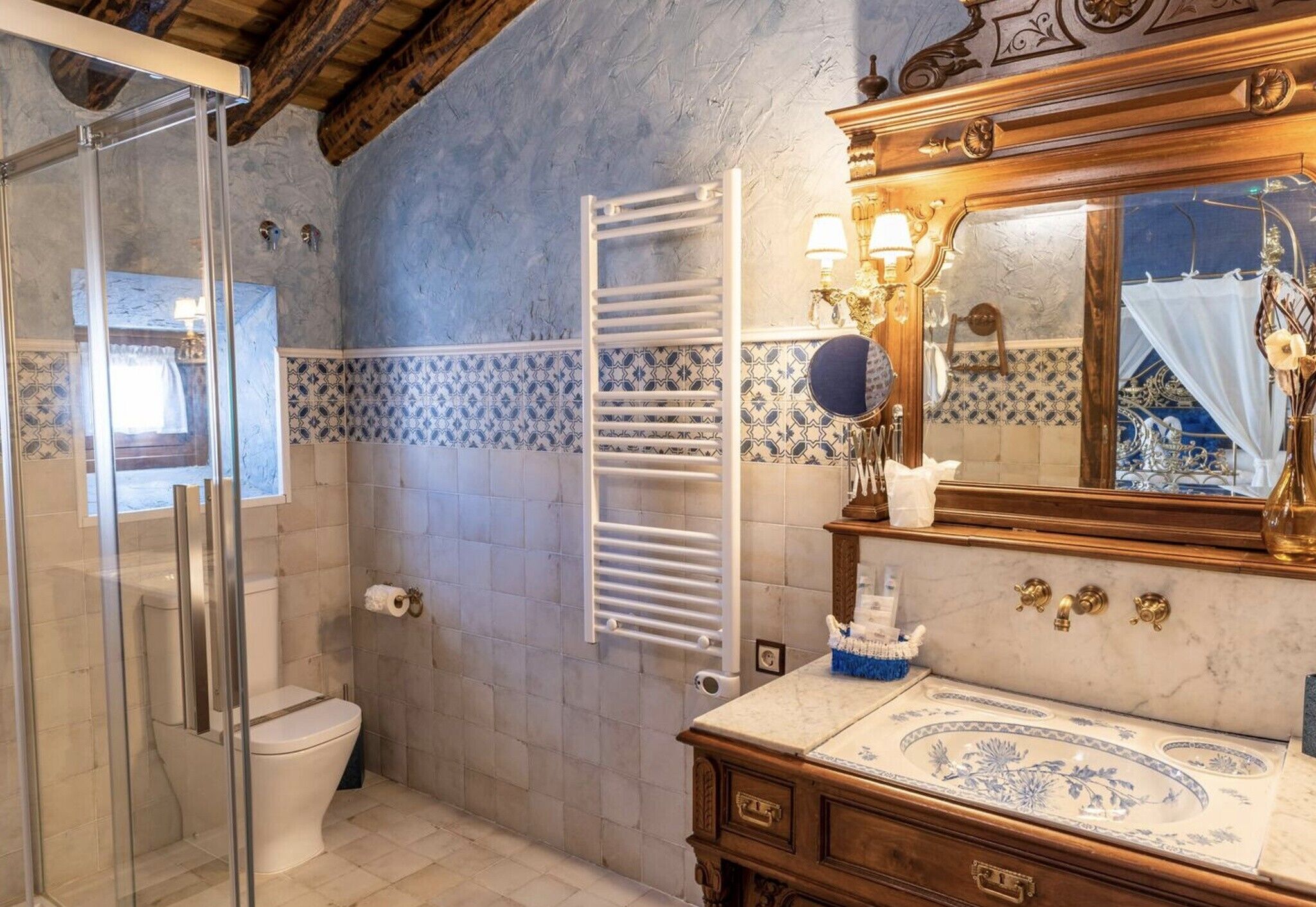 Un baño con cabina de ducha de vidrio, inodoro blanco, toallero, tocador con espejo y azulejos estampados.