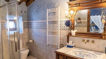 Un baño con cabina de ducha de vidrio, inodoro blanco, toallero, tocador con espejo y azulejos estampados.