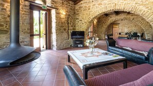 Une pièce aux murs de pierre, avec une cheminée, un canapé, une table ornée d’un vase et un téléviseur.