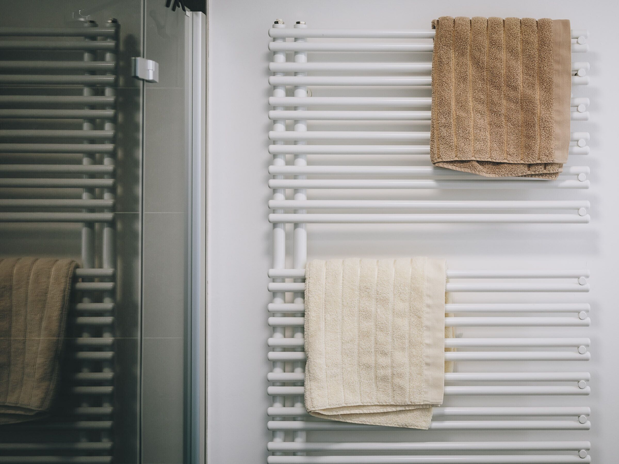 A bathroom with a glass shower enclosure and a white towel rack with two towels.