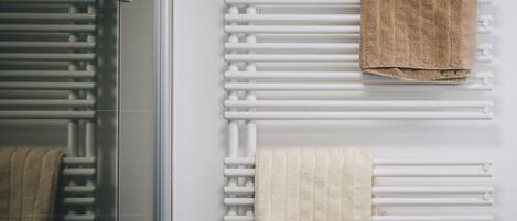 A bathroom with a glass shower enclosure and a white towel rack with two towels.