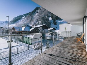A modern building with a wooden deck and glass railings overlooking a snowy mountain landscape. - Apartments Goldbergblick - TOP 3, City center & Balcony (Rauris)