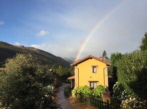A yellow house with a garden path leading to it, surrounded by greenery and hills. - Country House 'Los Avellanos 2' with Mountain Views, Private Terrace and Garden (Celis)