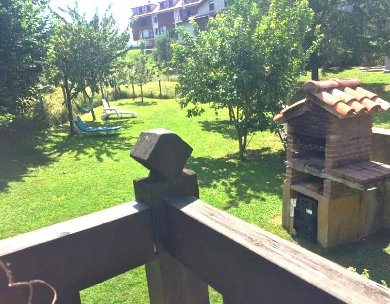 A grassy area with a hammock, a brick barbecue, and a building in the background.