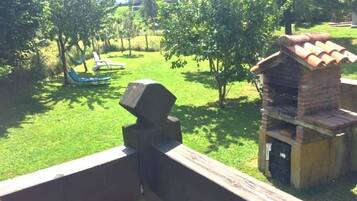 A grassy area with a hammock, a brick barbecue, and a building in the background.