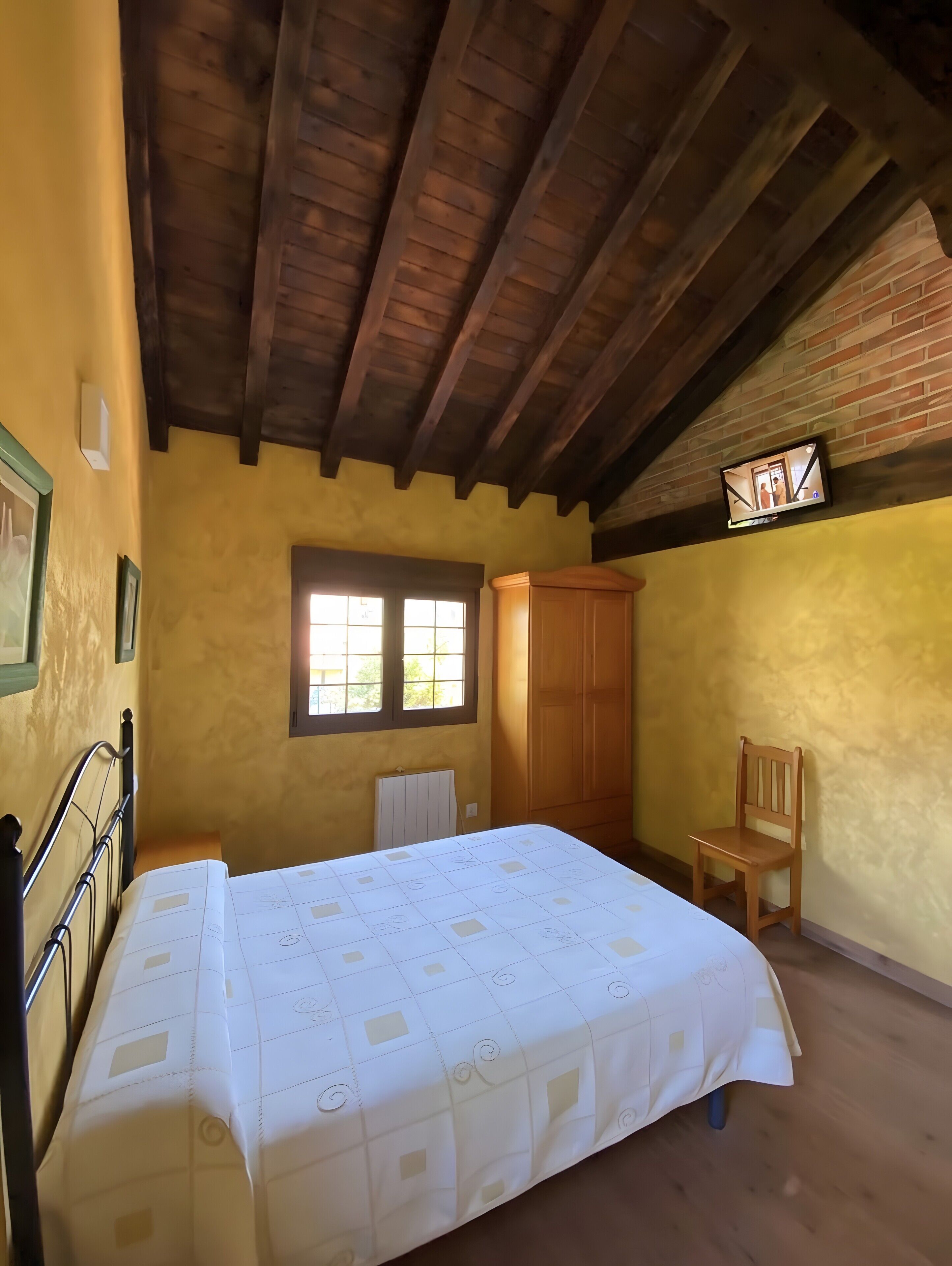 A bedroom with a bed, a wooden chair, a wardrobe, and a window.