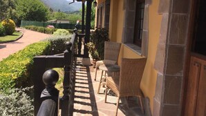 A building with a balcony, wicker chairs, and a view of a landscaped garden and mountains. - Country House 'Los Avellanos 2' with Mountain Views, Private Terrace and Garden (Celis)