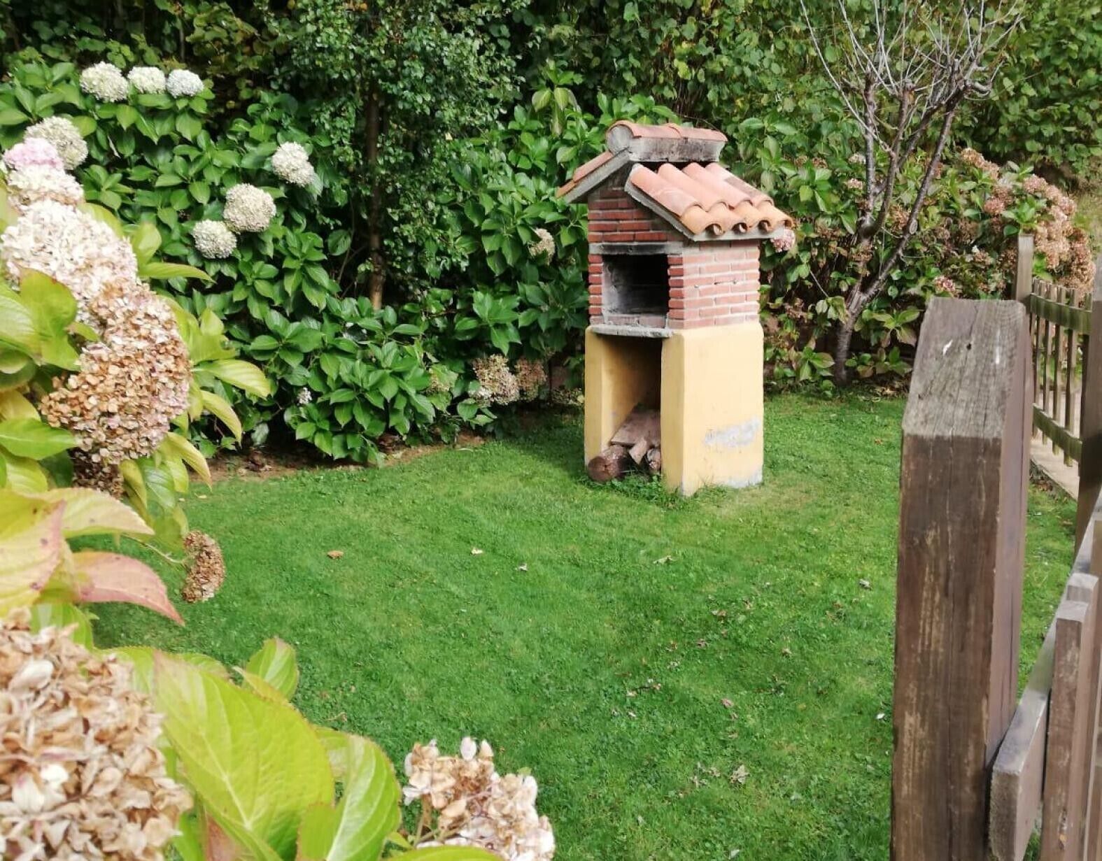 A brick birdhouse with a tiled roof in a garden.