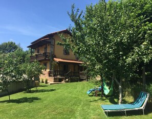 Uma casa de dois andares com varanda, gramado e rede.