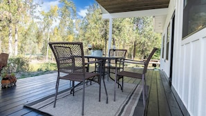 Un patio exterior con mesa y sillas, rodeado por una terraza de madera y vistas a árboles.