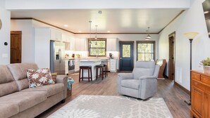 Un amplio salón con un sofá, un sillón gris y una cocina al fondo.