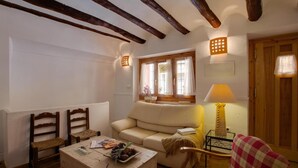 Ein gemütliches Wohnzimmer mit einer Couch, zwei Holzstühlen, einem Couchtisch mit Dekoration, einer Lampe und einem Fenster mit Vorhängen.