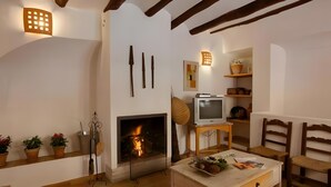 Ein gemütliches Wohnzimmer mit Kamin, Holzbalken, Fernseher und Esstisch.