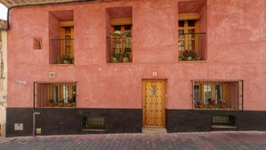 Ein pinkfarbenes Gebäude mit einer Holztür, Fenstern mit Metallgitter und Blumenkästen.